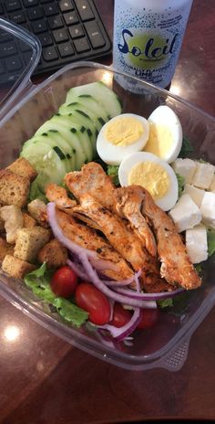 a salad in a plastic container with chicken, cucumber, tomatoes and boiled eggs