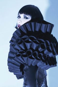 a woman with black hair and makeup is holding a fan shaped object in her hands