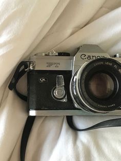 an old camera sitting on top of a bed next to a white blanket and black strap