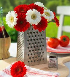 red and white flowers sit in a vase on a table with plates, napkins and utensils