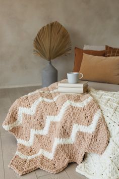 a coffee cup sits on top of a crocheted blanket next to a book