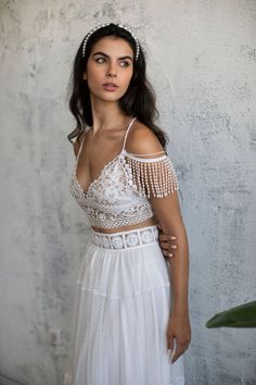 a woman in a white dress standing next to a wall with her hands on her hips