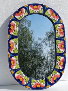 a colorful mirror hanging on the side of a white wall next to trees and bushes