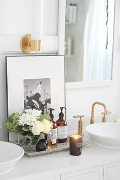 a bathroom vanity with flowers, candles and pictures on the counter top in front of a mirror