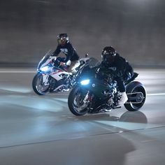 two motorcyclists are riding down the street at high speeds with their lights on