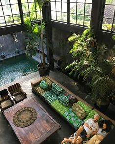 two men sitting on couches in an indoor living room with pool and trees behind them