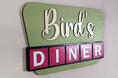 a sign that says birds diner hanging on the side of a white wall with pink lettering