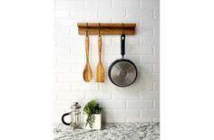 two wooden utensils hanging on a brick wall next to a pot and spatula