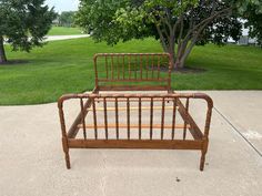 a bed frame sitting on top of a sidewalk next to a green field and trees