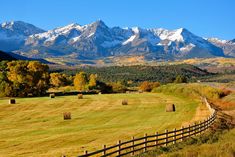 a field with mountains in the background and bales on the grass by it's fence