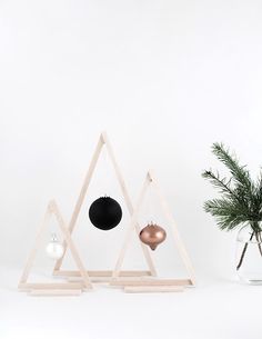 two ornaments are on display in front of a white wall and a plant with pine branches