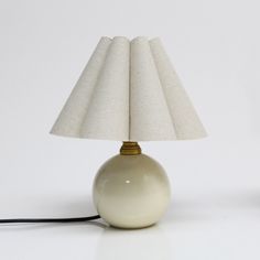 a white table lamp with a beige shade on it's base and a black cord