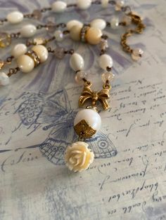 This creamy, dreamy little assemblage necklace is made from vintage pieces and new for delightful look! A vintage carved flower dangles from a lustrous white freshwater pearl and vintage gold tone bow for the centerpiece. The rest of the necklace is made up of Czech glass beads, faceted crystals, vintage mother of pearl with rhinestone spacer beads, tiny vintage glass jewels, cathedral beads and more! The necklace is adjustable in length from 19 1/4 inches to 21 1/4 inches and closes with a lobs Vintage Cream Pearl Drop Necklace, Elegant Vintage Charm Dangle Necklaces, Vintage Dangle Pearl Drop Necklace, Vintage Pearl Drop Dangle Necklace, Vintage Pearl White Pearl Necklace Gift, Vintage Pearl White Pearl Necklace For Gift, White Vintage Necklace For Vintage Collection, White Vintage Necklace With Vintage Charm, Vintage White Pearl Necklace