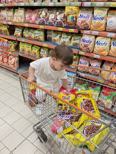 a young child pushing a shopping cart in a grocery store filled with cereal and snacks