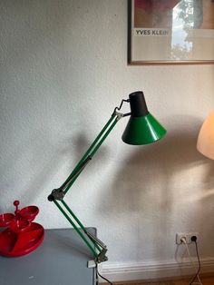 a green lamp sitting on top of a table next to a red bowl and white wall