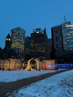 the city skyline is lit up at night with lights on it and snow covered ground