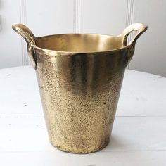 a gold colored metal bucket sitting on top of a white table next to a wall