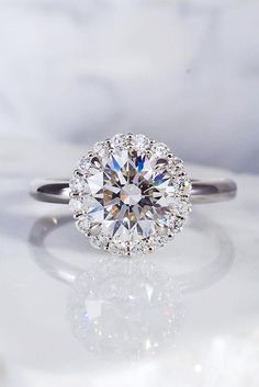 an engagement ring with a center diamond surrounded by small round brilliant cut diamonds on a white marble surface