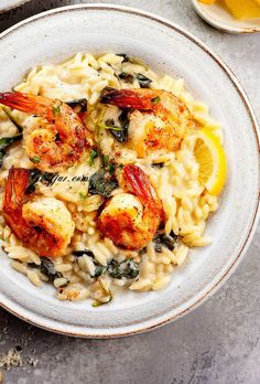 pasta with shrimp and spinach in a white bowl next to lemon wedges on the side