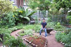 a man standing in the middle of a garden with lots of plants and trees around him