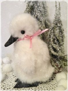 a small white duck with a pink ribbon around its neck sitting next to a tree