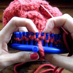 two hands are holding a blue and red comb with yarn on it, while another person is knitting