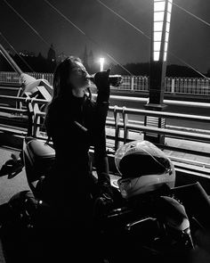 a woman drinking from a bottle while sitting on a motorcycle at night with the lights turned on