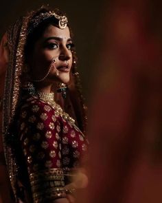 a woman in a red and gold bridal outfit looks into the distance with her eyes closed