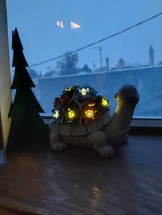 a small turtle with lights on its back sitting next to a christmas tree in front of a window