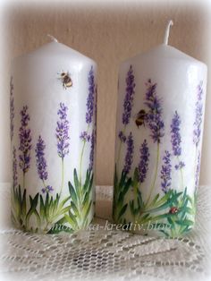 two white candles with purple flowers and bees on them are sitting next to each other