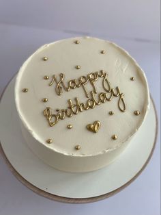 a white birthday cake with gold letters and hearts on the top that says happy birthday