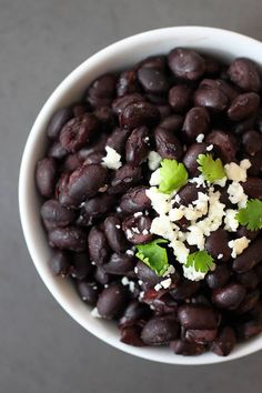 a white bowl filled with black beans covered in feta cheese and cilantro