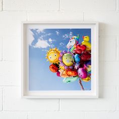 a white frame hanging on a brick wall with balloons in the shape of animals and birds