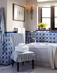 a bathroom with blue and white tiles on the walls, tub and chair in it