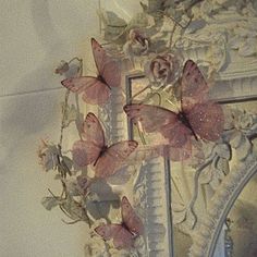 some pink butterflies are hanging on the wall next to a mirror with flowers and leaves