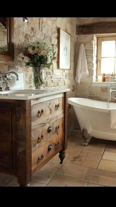 a white bath tub sitting under a window next to a wooden sink vanity with drawers