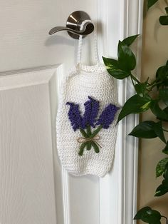 a crocheted bag hanging on a door handle with purple flowers in the front