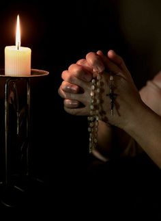 a person holding a rosary with a lit candle in the background