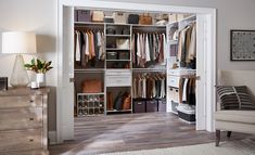 an open closet with clothes on shelves and drawers in the corner, next to a chair