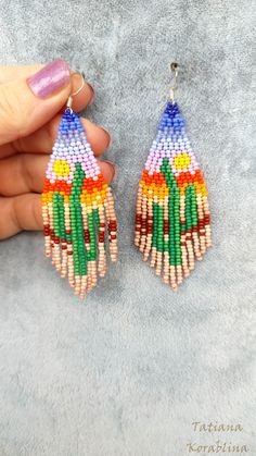 a pair of colorful beaded earrings on top of a gray surface with a woman's hand holding it