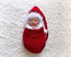 a newborn baby wearing a santa hat and sleeping in a red bag on a white blanket