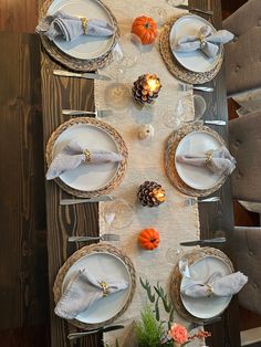 the table is set for thanksgiving dinner with white plates and silverware, pine cones, and candlesticks