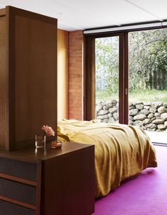 a bed sitting next to a window in a bedroom under a purple rug on top of a wooden dresser