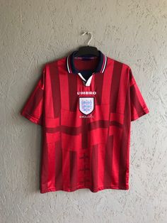 a red shirt hanging on a wall with a hanger in front of it that says umbro