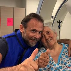 an older woman giving the thumbs up sign next to a man in a blue shirt