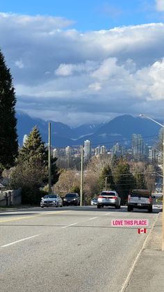 cars are parked on the side of an empty street with mountains in the background and a sign that says love this place