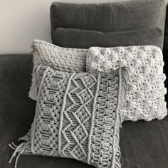 two crocheted pillows sitting on top of a gray couch next to each other