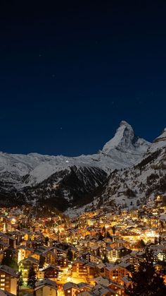 the city is lit up at night with mountains in the background and snow on the ground