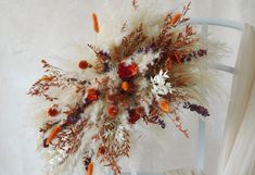 an arrangement of dried flowers and feathers on a chair in front of a white wall