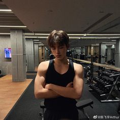 a young man standing in front of a row of exercise machines with his arms crossed